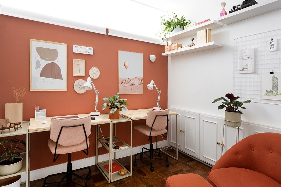 Escritório home office com parede colorida, mesa de madeira e cadeira de escritório rosa. 