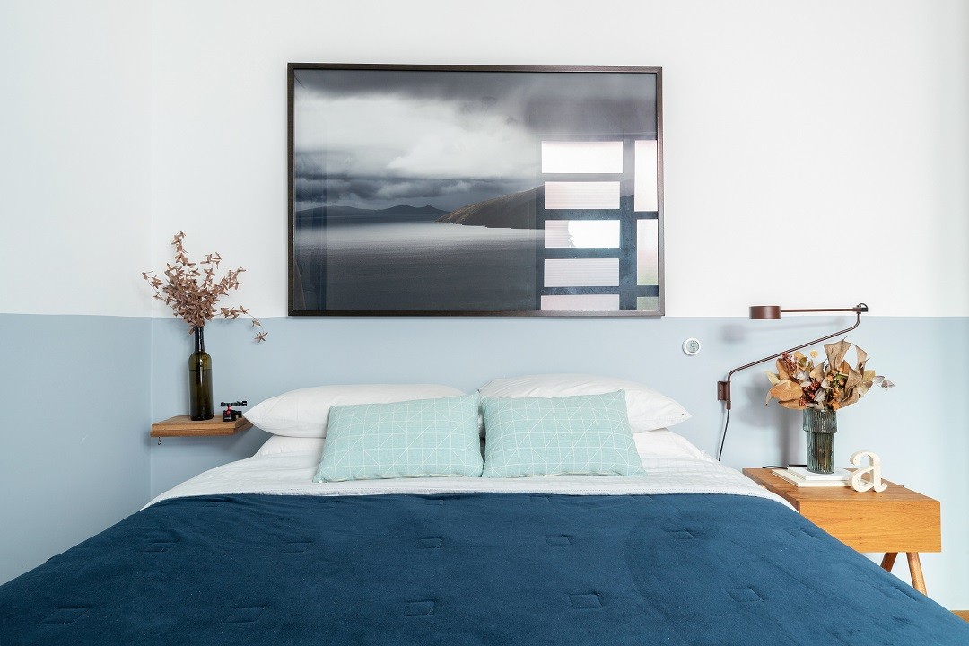 Quarto azul com pintura meia parede, decoracão azul, móveis de madeira, flores e roupa de cama azul.
