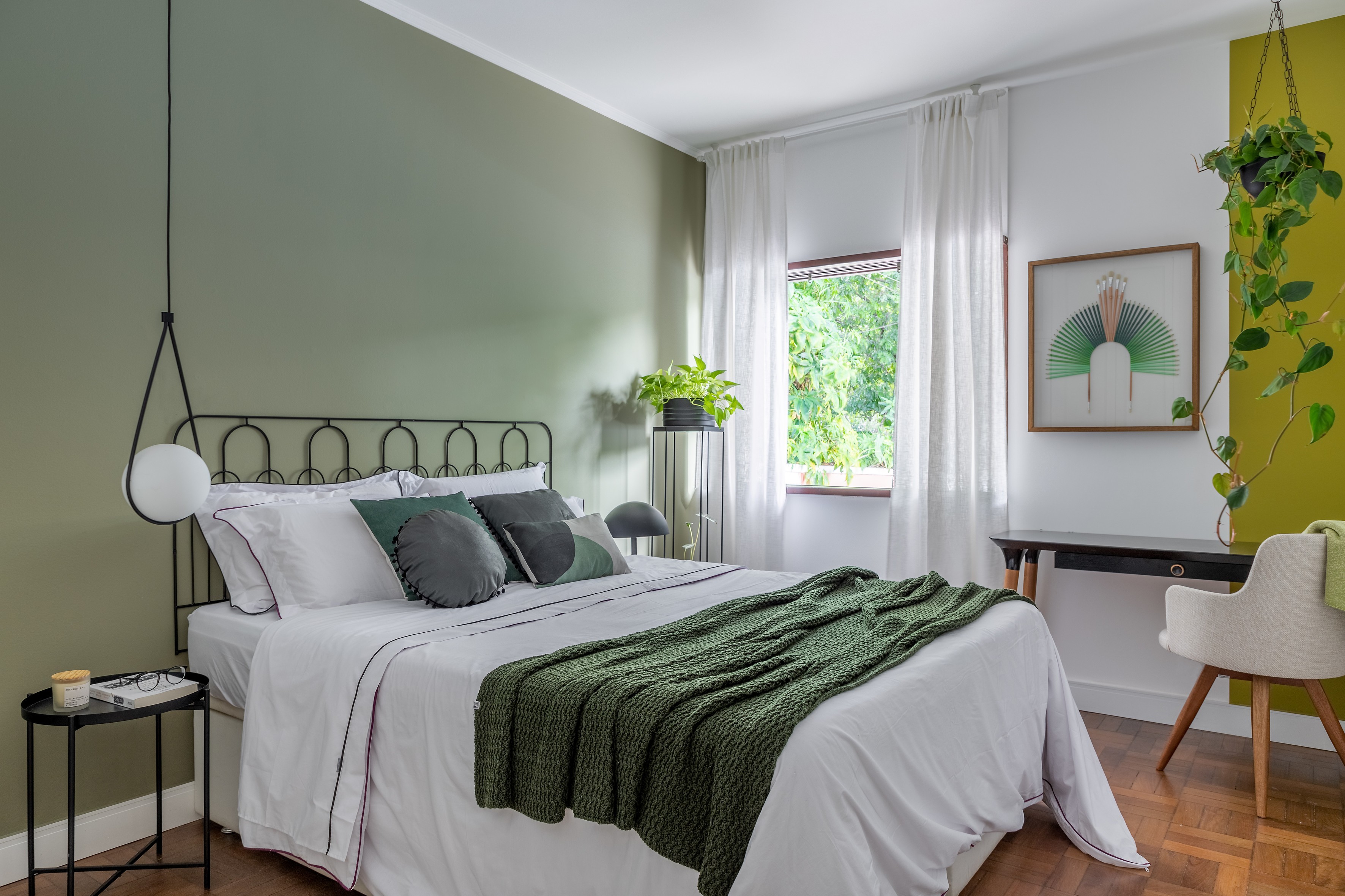 Quarto verde com parede verde, cama com roupa de cama branca e verde, pintura setorizada verde, plantas no quarto, parede branca, teto branco e piso de madeira.