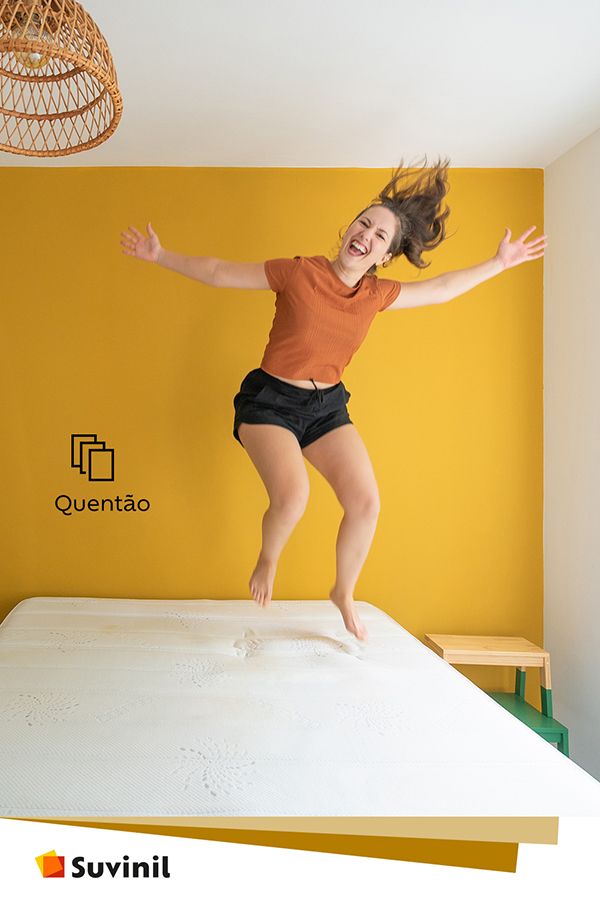 Karla Amadori alegre pulando na cama e a parede na cor quentão da Suvinil