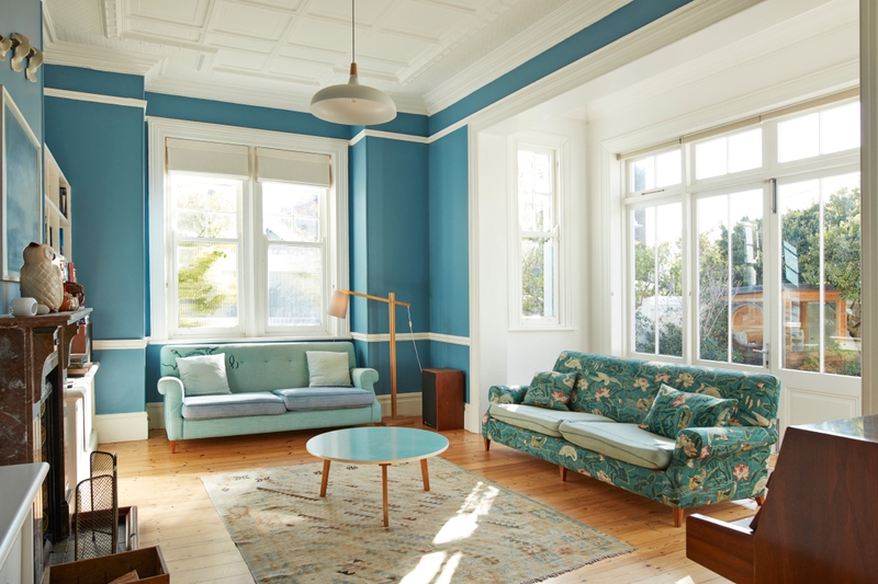 Sala de estar com janelas e iluminação natural. Uma das paredes está pintada com azul Suvinil e a outra de branco.