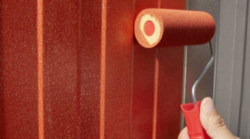 profissional aplicando tinta vermelha com rolo em portão de metal