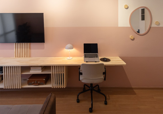 sala com parede tricolor monocromática rosa com cadeira em frente a rack com computador e TV representando cores de tinta semi brilho