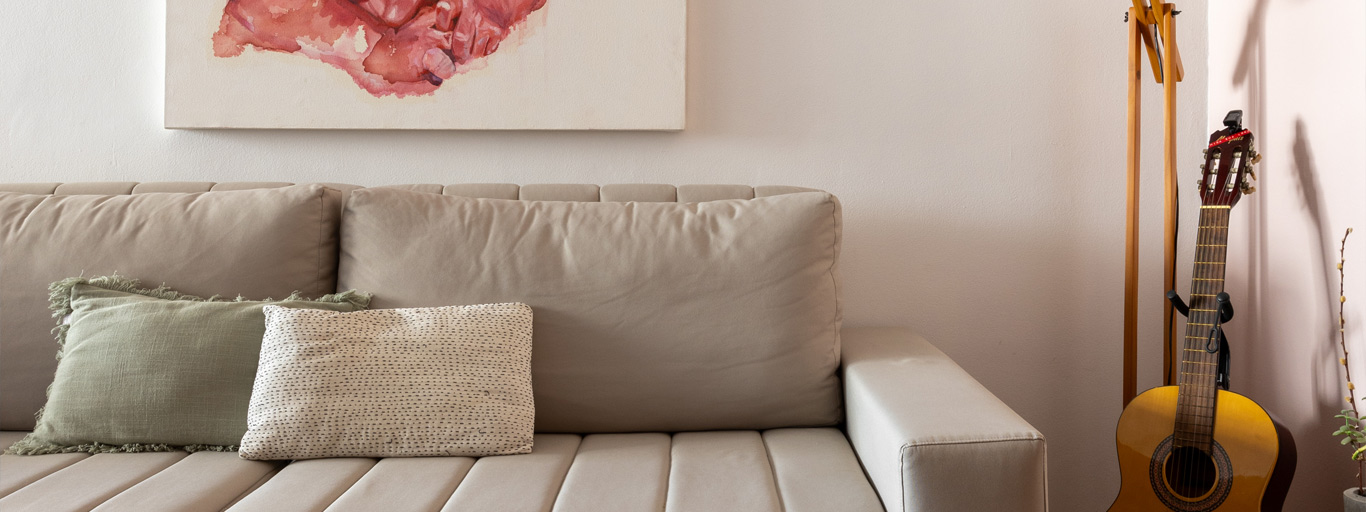 sofá bege em frente a parede clara representando qual a melhor tinta lávavel para parede interna