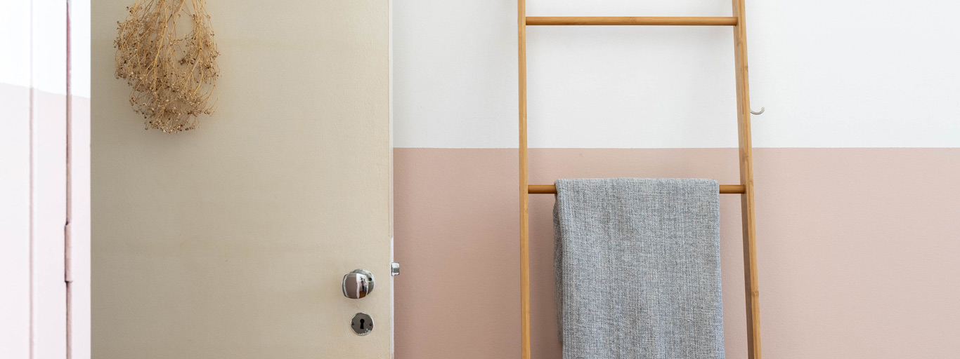 parede bicolor branca e rosa com porta rosa e escada de madeira com toalha pendurada representando tinta fosca ou acetinada
