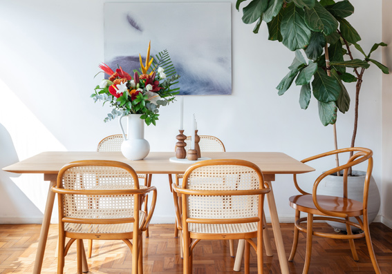 sala de jantar decorada com mobilia demadeira com vaso de flores e parede branca com quadro 