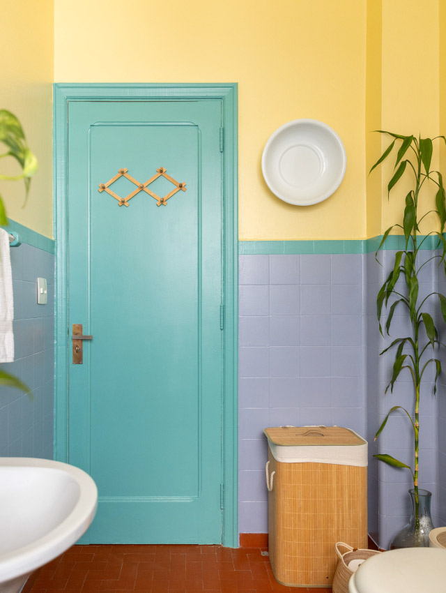 Imagem de um banheiro com paredes roxas, amarelas e porta verde-água